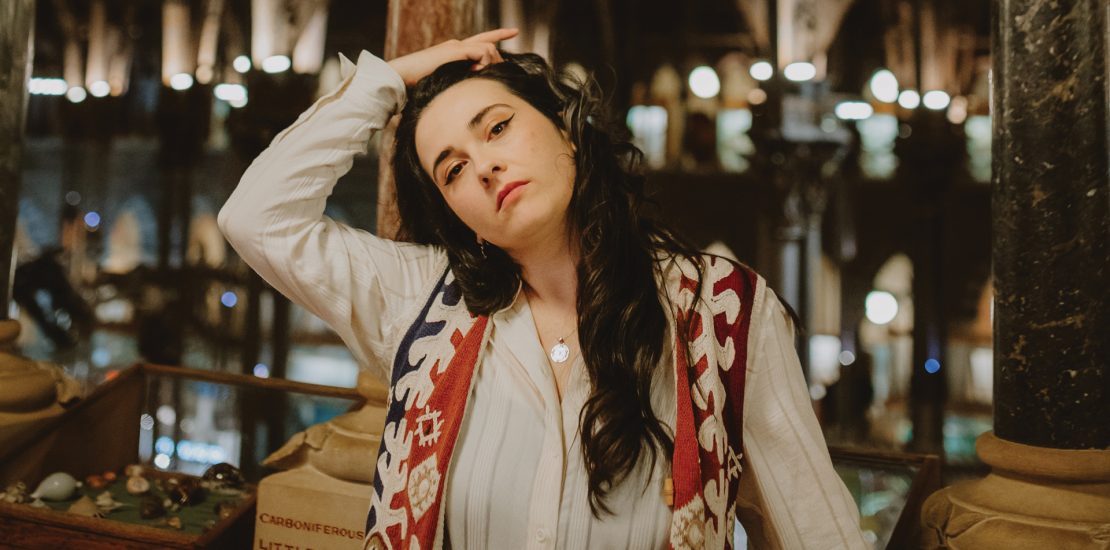 Olivia Rafferty stands in a a museum posing with her hand in her hair.