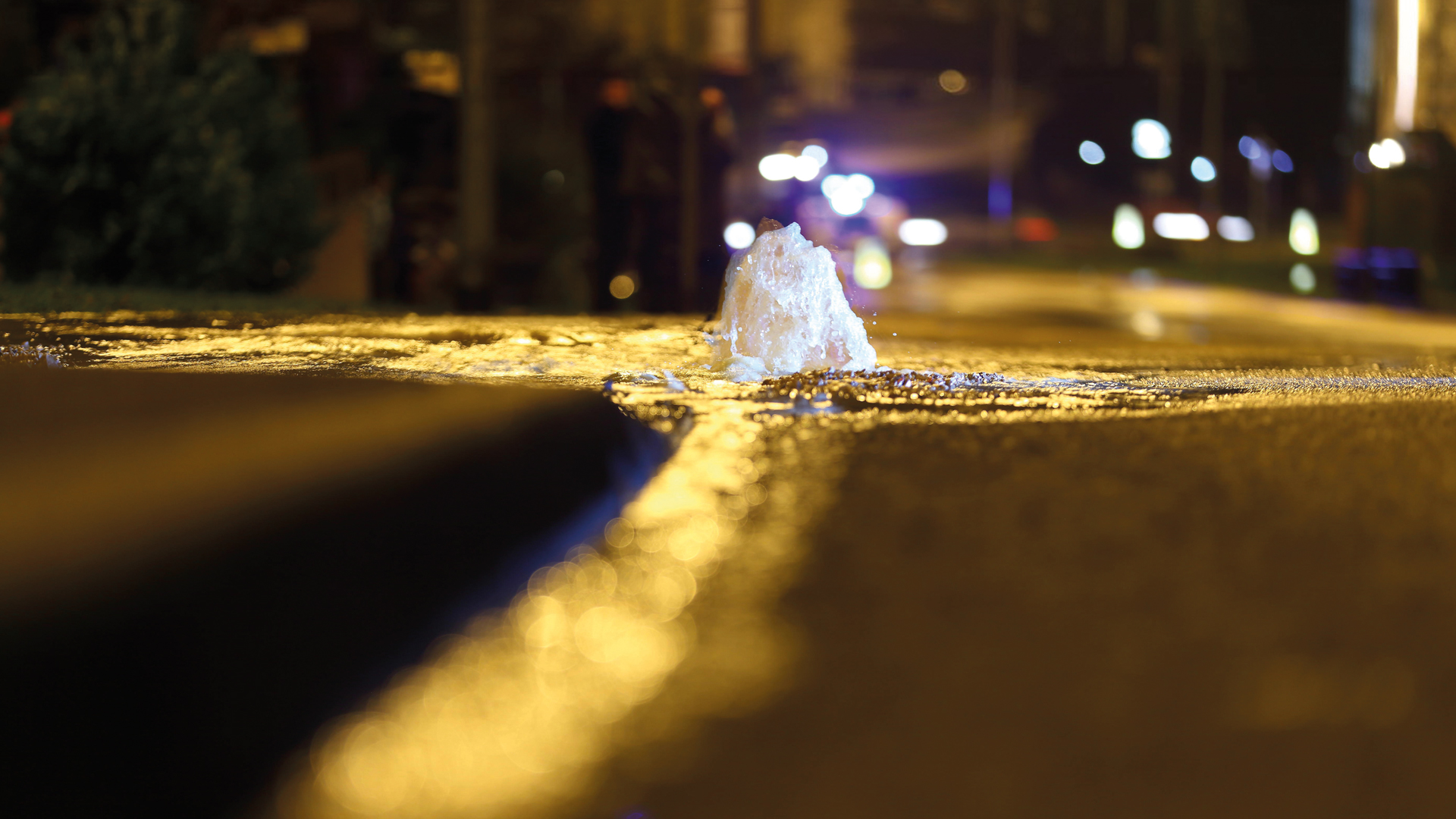 A burst water main erupts from beneath a road
