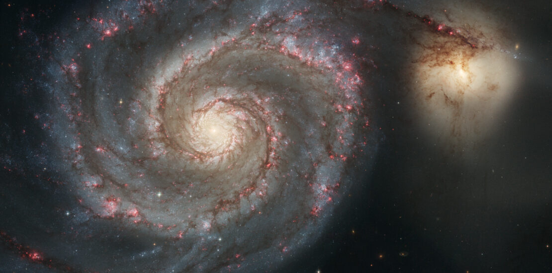 Telescope image of a spiral galaxy with a small companion galaxy branching off.
