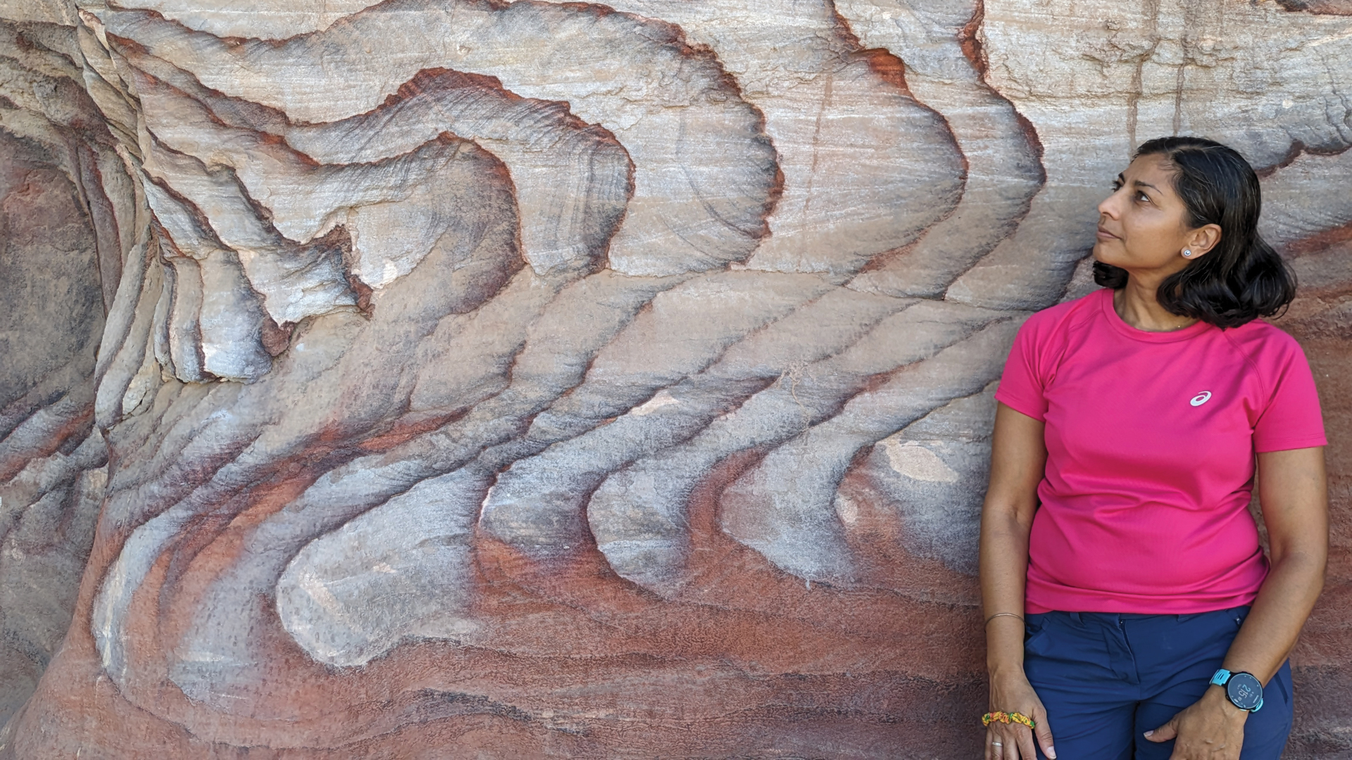 A woman stands looking at a cliff face with wiggles in the rock.